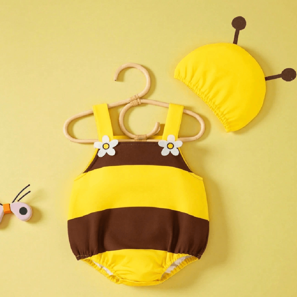 A baby bee-themed two-piece outfit set featuring a yellow and brown striped romper with white flower details on the straps, displayed on a wooden hanger, alongside a matching yellow bee cap on a solid pale yellow background.