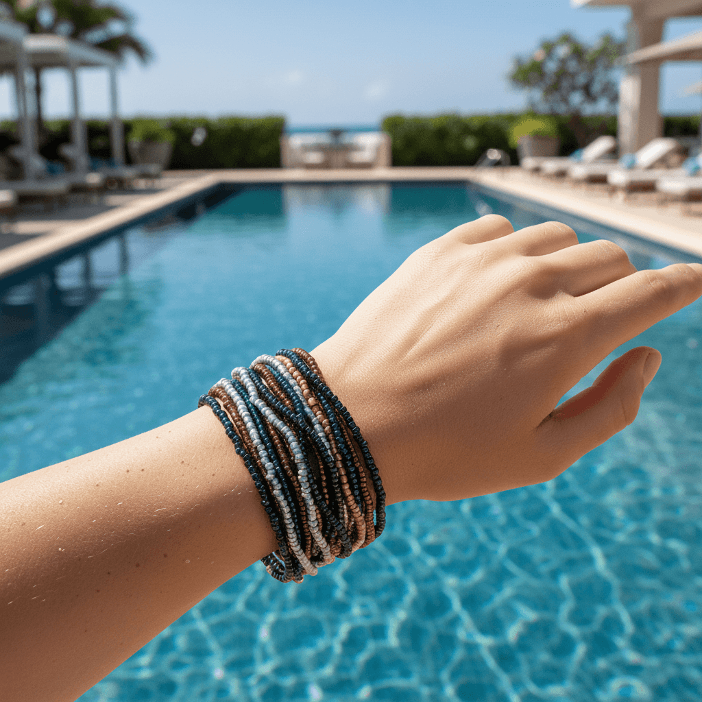 A close-up of a person's wrist wearing a stack of multi-colored beaded bracelets, set against a blurred background of a swimming pool and resort patio.