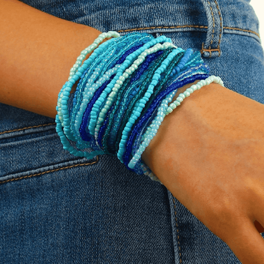 Close-up of a wrist wearing multiple blue beaded bracelets against a denim background