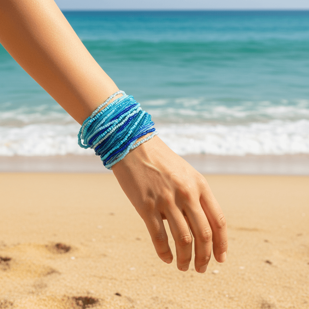 Hand wearing a blue beaded bracelet on a beach with ocean in the background