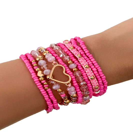 Pink beaded bracelet with a heart charm on a wrist against a white background