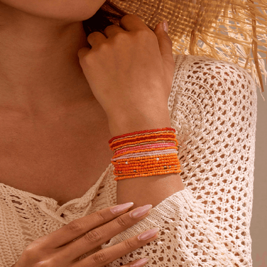 Close-up of a person's arm wearing multiple colorful beaded bracelets against a neutral background.