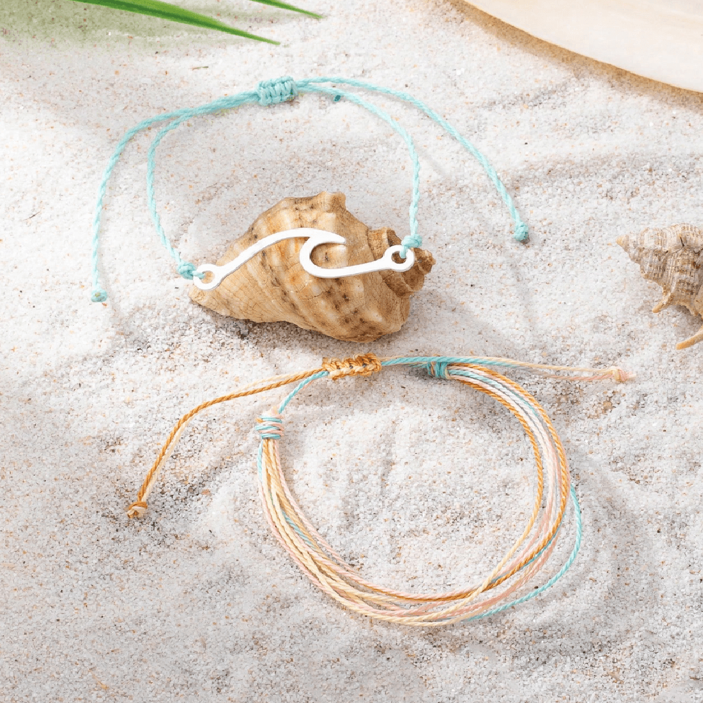 Two bracelets on sand with shells in the background