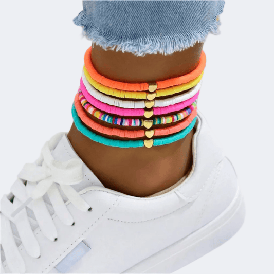Colorful bracelets on a person's wrist with a white sneaker and denim jeans.