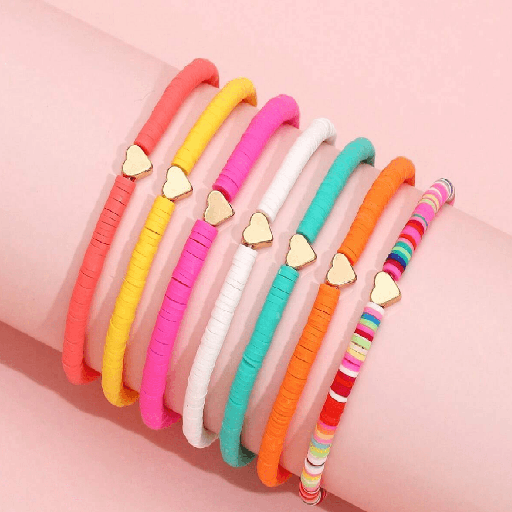 Colorful bracelets with heart-shaped charms on a pink background