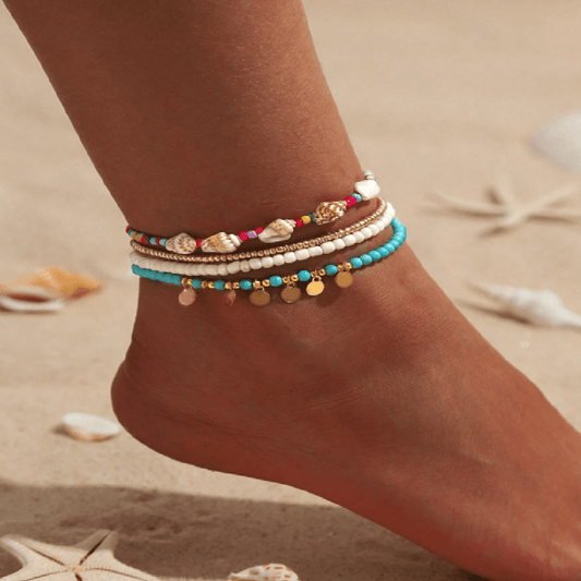 Colorful beaded anklets on a foot with a sandy background