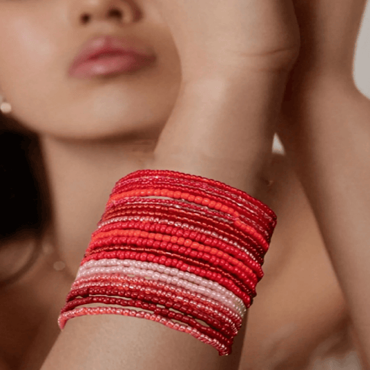 Close-up of a woman's arm with multiple red and pink bracelets on a blurred background