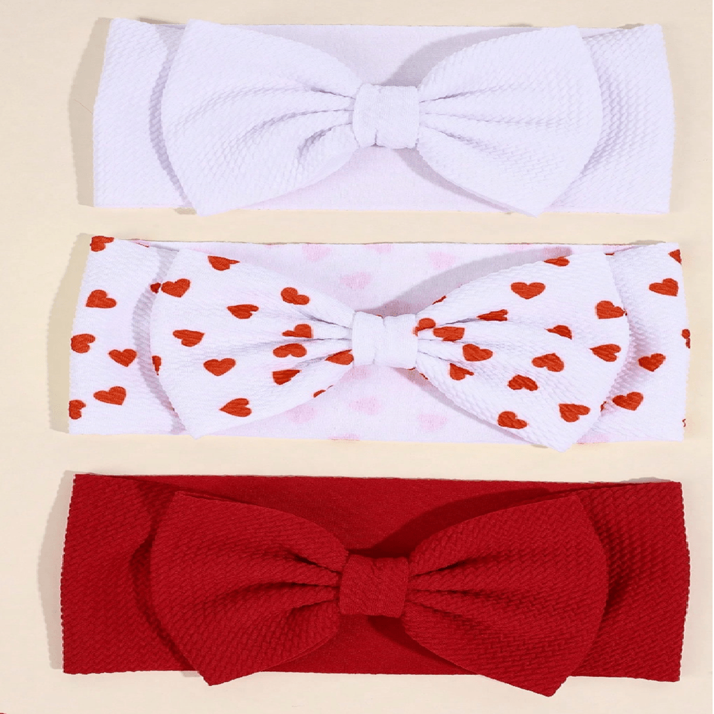 Three textured fabric headbands with large bows, arranged vertically on a light beige background. The top headband is solid white.