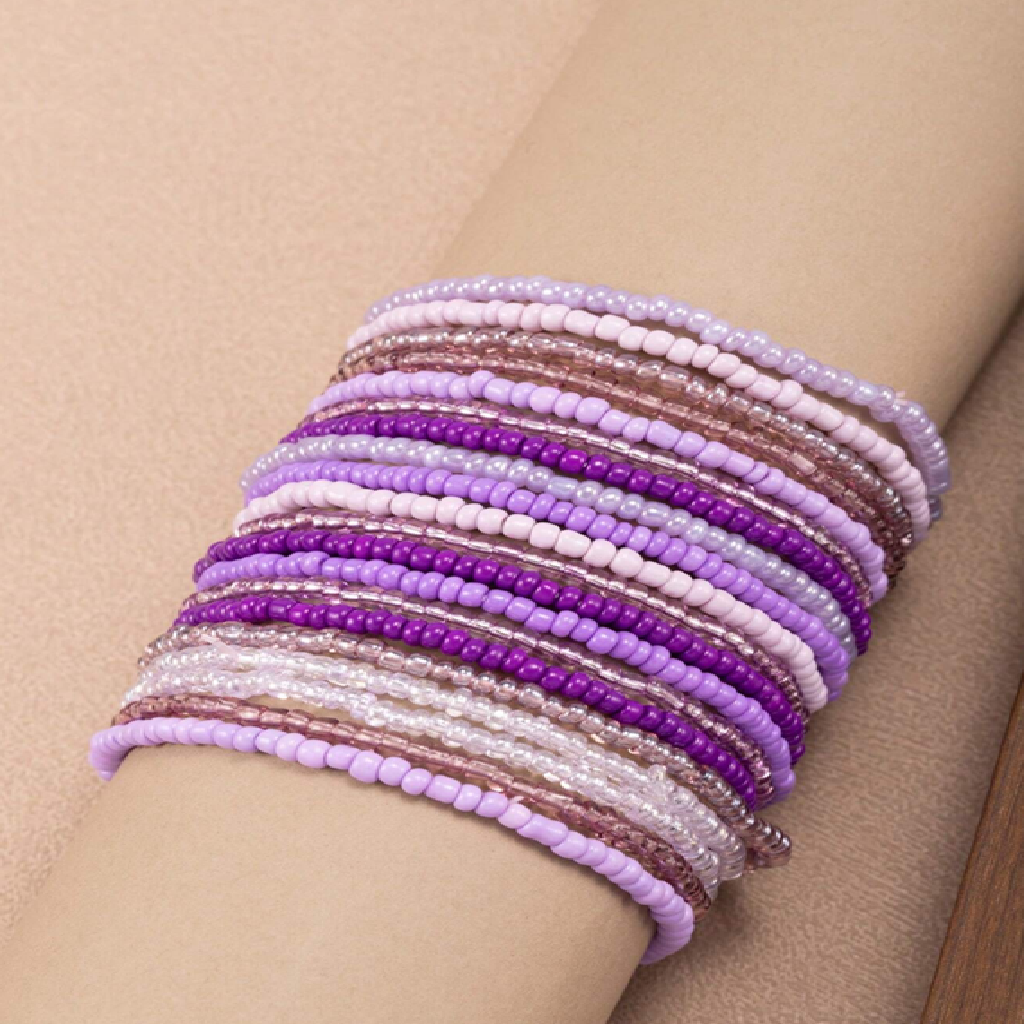 Multiple beaded bracelets in purple and pink on a wrist against a beige background