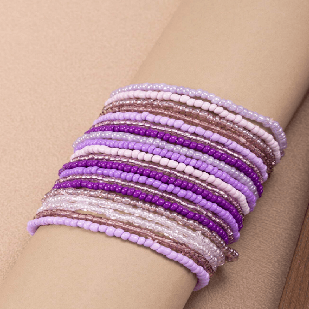 Stack of purple and pink beaded bracelets on a person's wrist against a beige background