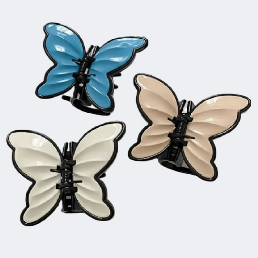 Three butterfly-shaped hair clips in blue, beige, and white on a light gray background.