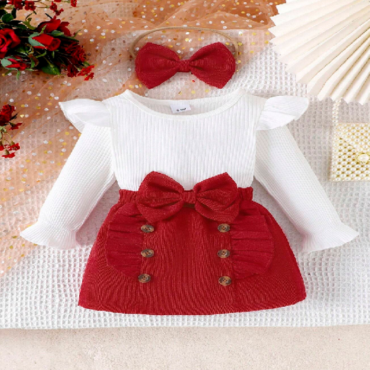 Baby outfit with white long-sleeve top and red knitted skirt with bow on a textured surface.