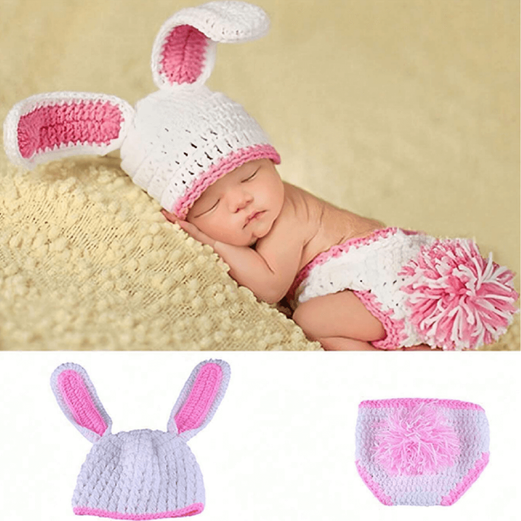 Newborn baby in a pink and white bunny outfit on a beige blanket.