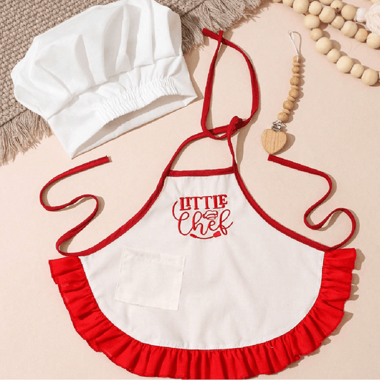 Children's apron with 'Little Chef' text, white chef hat, and wooden beads on a beige background