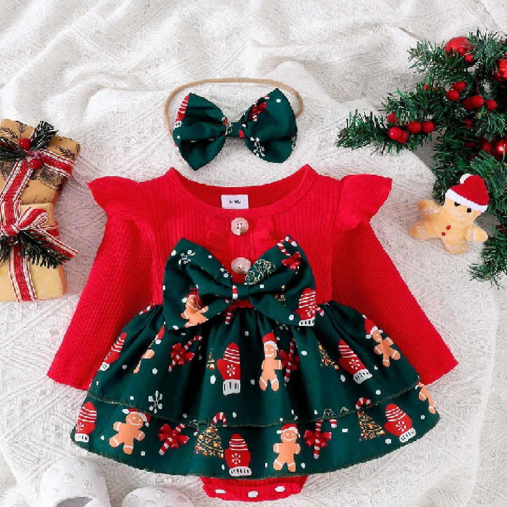 Christmas-themed baby outfit with red top and green skirt, headband, and decorations on a textured surface.