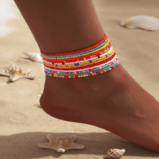 Colorful beaded anklets on a foot with a sandy background
