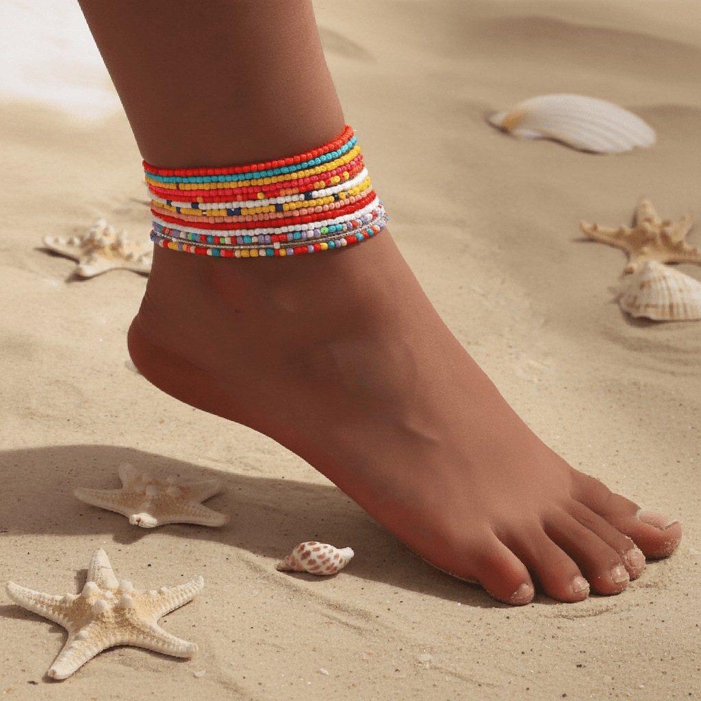 Colorful beaded anklets on a foot with sand and shells in the background