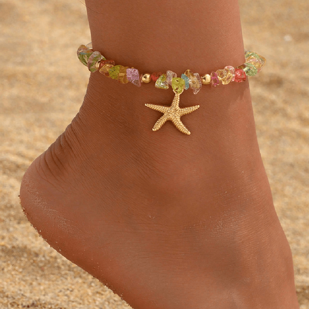 Colorful beaded anklet with a starfish charm on a foot against a sandy background