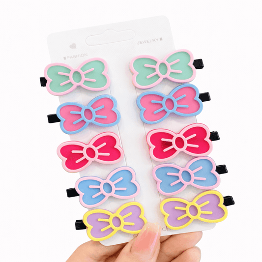 Set of colorful bow-shaped hair clips on a white card held by a hand.