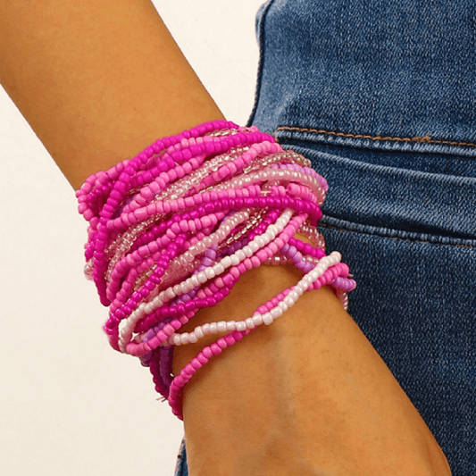 Close-up of a wrist wearing multiple pink beaded bracelets with a blurred background.