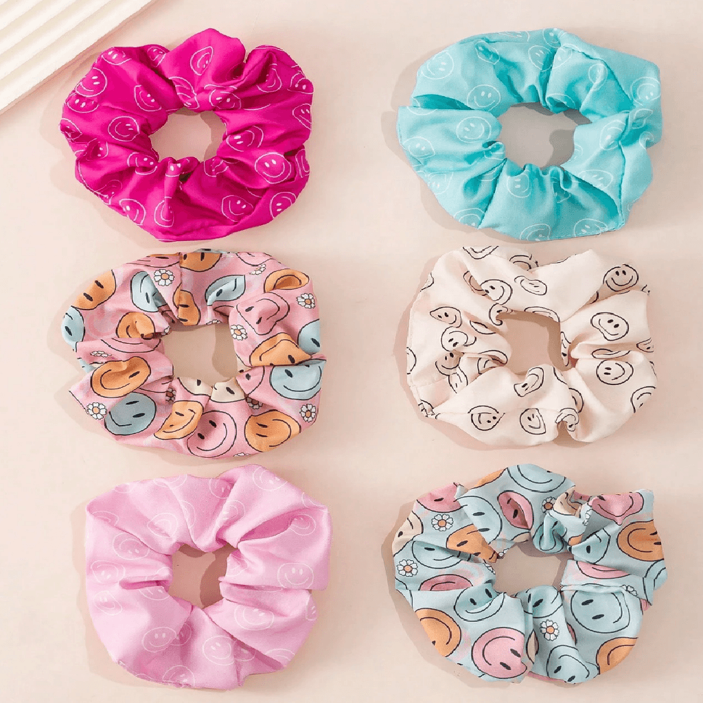 Six fabric hair scrunchies arranged in a 2x3 grid on a light beige background. The top row features one bright pink scrunchie with a white swirl pattern and one light blue scrunchie with a white swirl pattern.