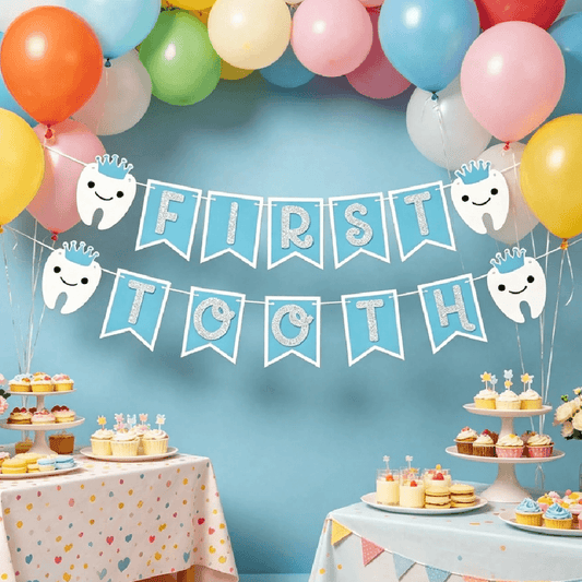 First tooth celebration with balloons, banner, and dessert table against a blue wall.