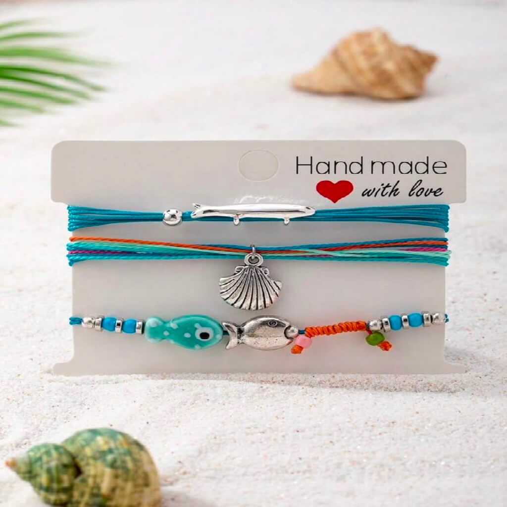 Set of colorful bracelets with charms on a 'Handmade with Love' card, surrounded by shells.