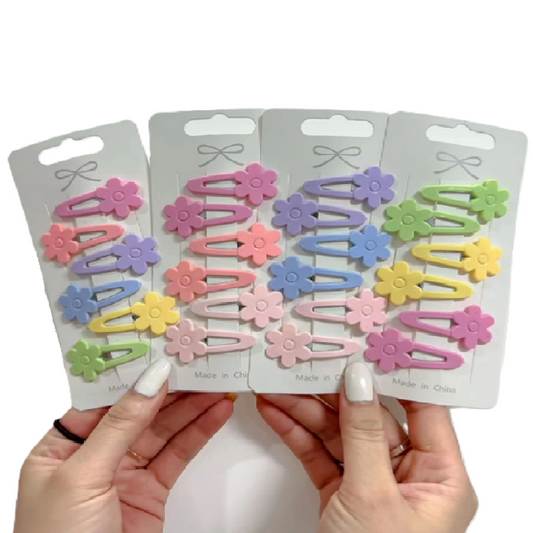 Four packages of colorful flower-shaped hair clips held by hands against a white background