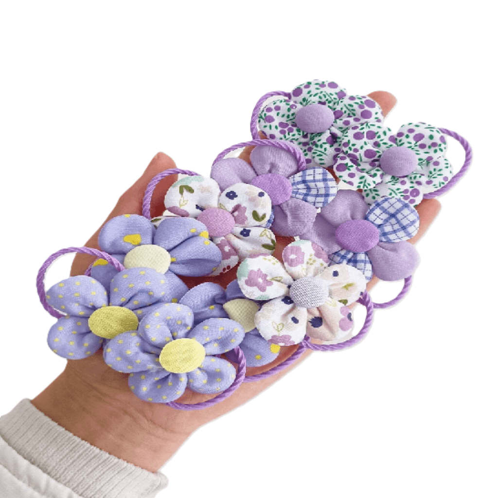 Hand holding a collection of decorative hair ties with floral patterns on a white background