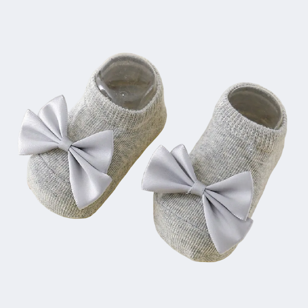 Gray baby shoes with large bows on a beige background