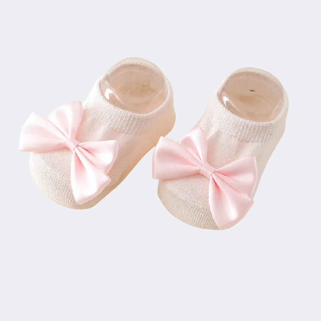 Pair of pink baby shoes with large bows on a light yellow background