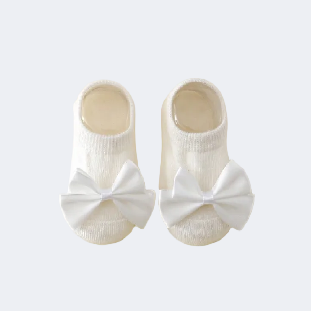 White baby shoes with large bows on a light gray background