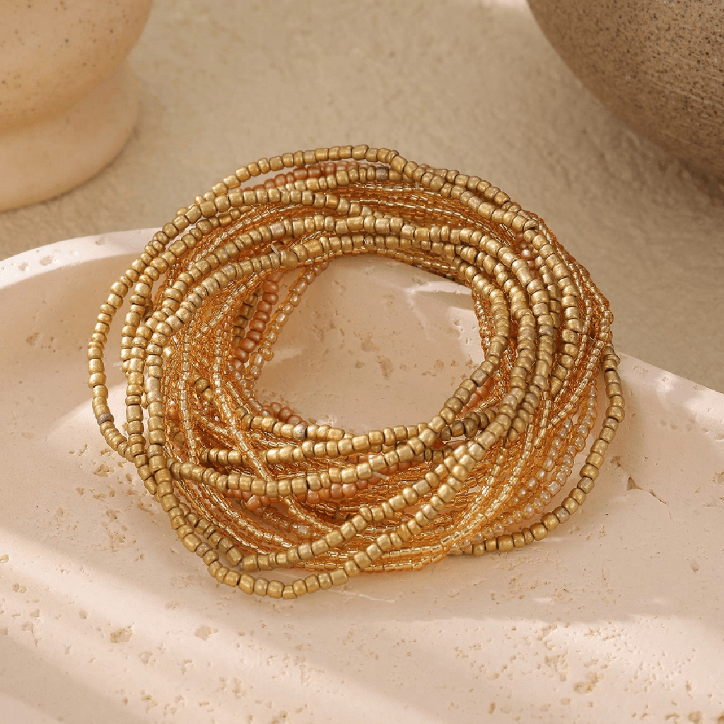 Coiled gold beaded bracelet on a textured beige surface