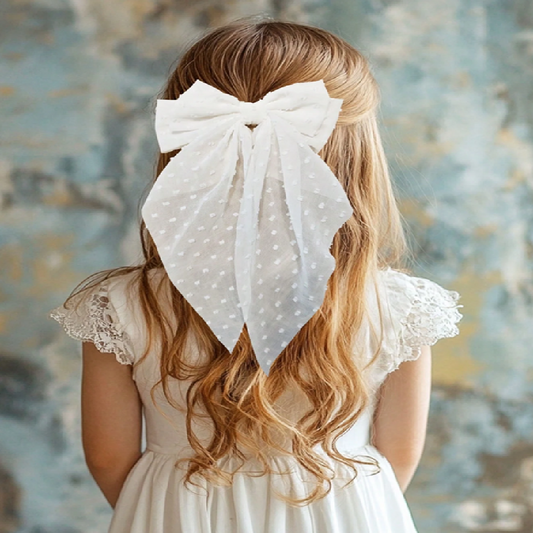 Person with long blonde hair wearing a large white polka dot bow in their hair, against a textured wall.