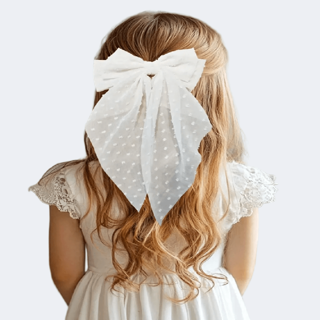 Woman with long blonde hair wearing a large white polka dot bow in her hair, against a plain background.