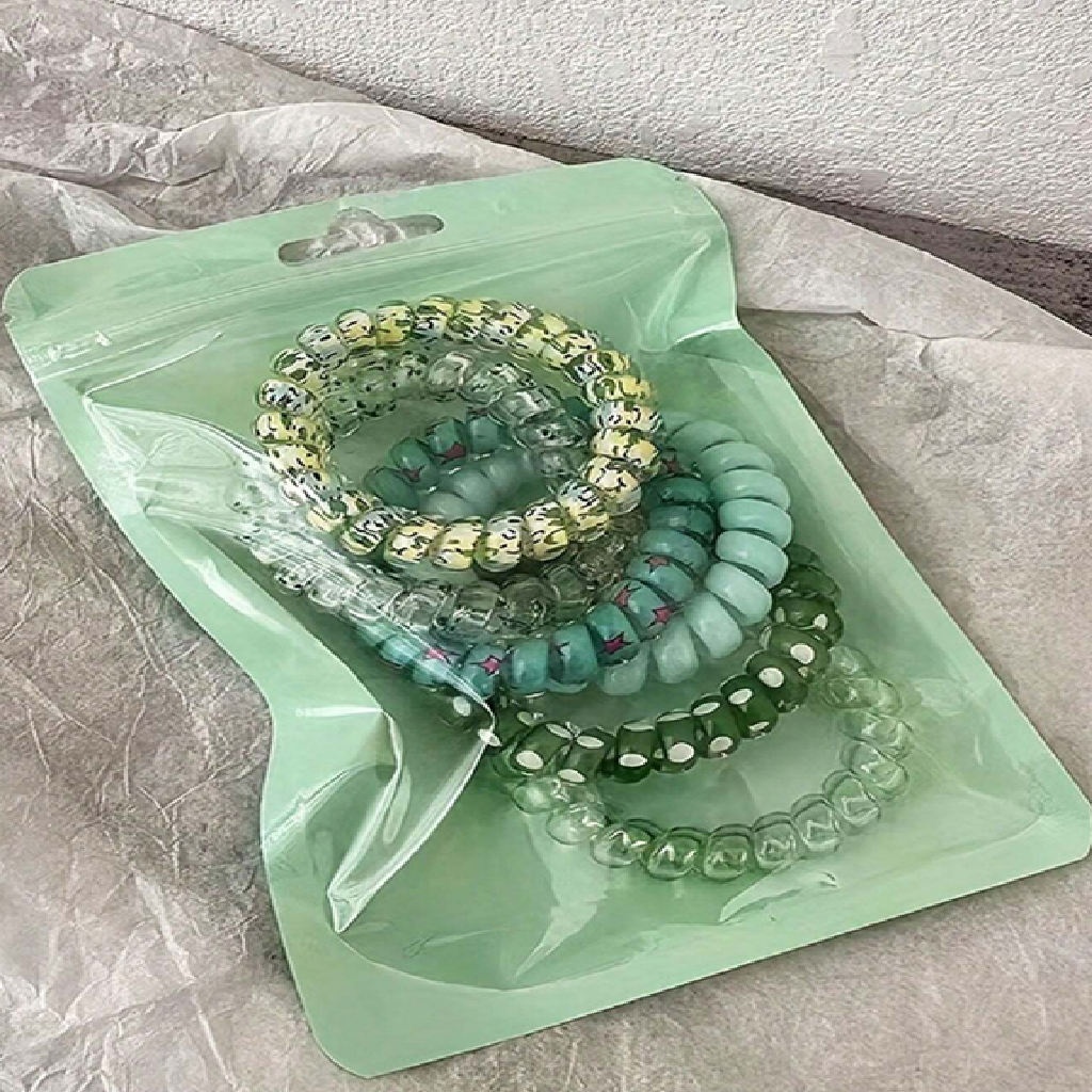 Set of colorful beaded bracelets on a green plastic bag with a textured surface background.