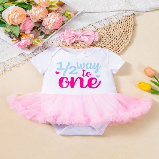 Baby outfit with '1/2 way to one' text and pink tutu on a light background with flowers and a hat.