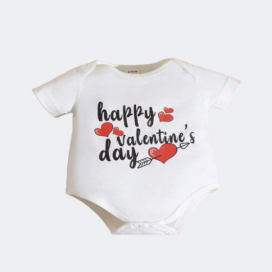 White baby onesie with 'Happy Valentine's Day' text on a textured surface with heart decorations.