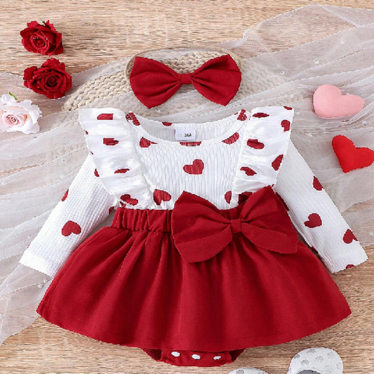 Children's outfit with red and white dress and headband on a wooden surface with flowers.