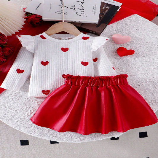 White top with red heart patterns and red skirt on a hanger with decorative items.