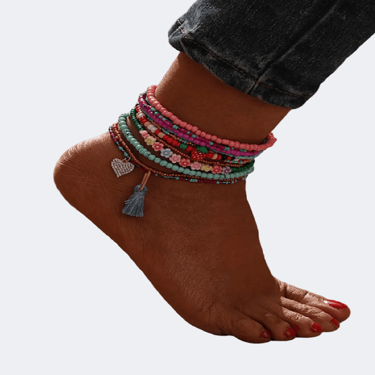 Colorful beaded anklets on a foot with a plain background