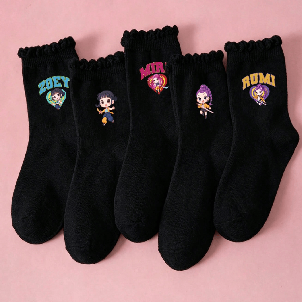 Five pairs of black crew socks with scalloped ruffle hems are arranged in a fan shape on a solid pink background. Each pair features a different colorful embroidered cartoon character and text: 'ZOEY', 'MIRA', 'RUMI', and others.