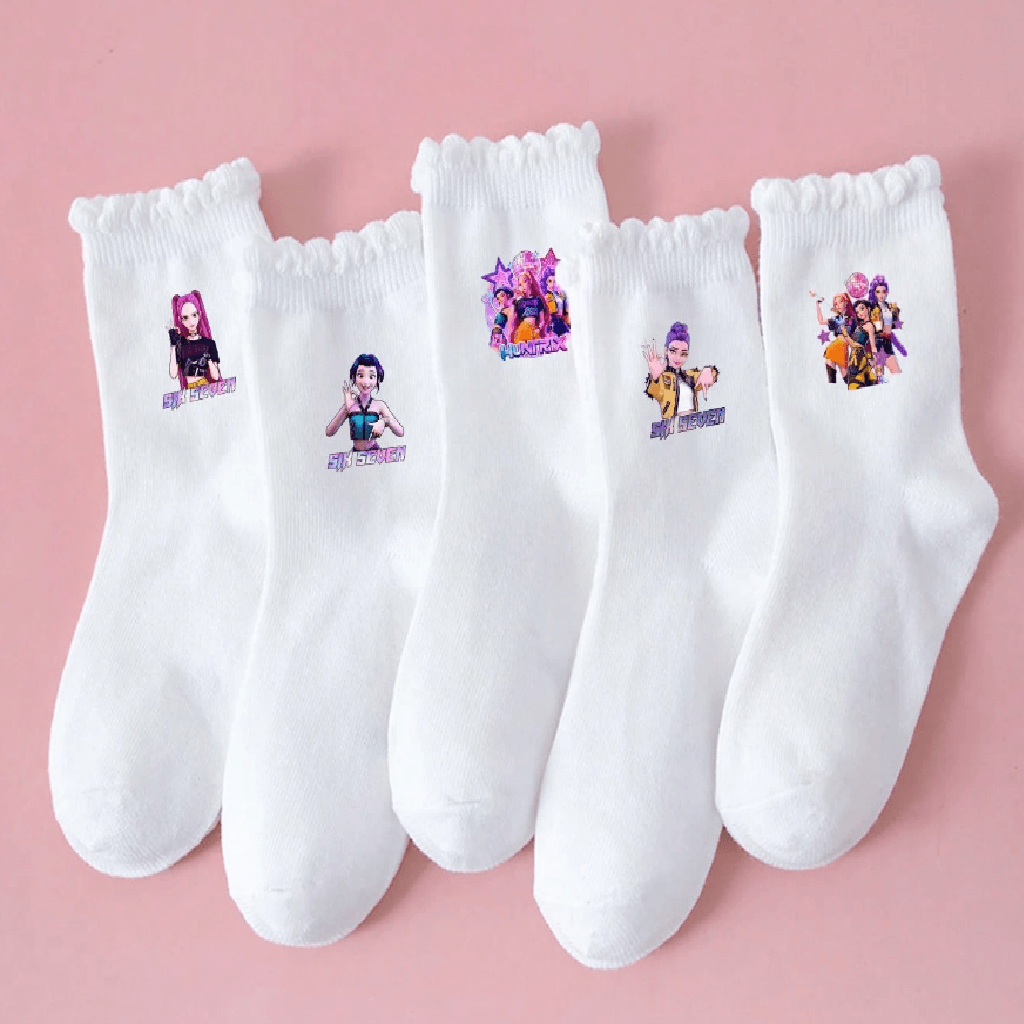 Five white crew socks with ruffled cuffs are arranged in a fan shape on a solid pink background. Each sock features a small colorful printed graphic of a female cartoon character with text below it.