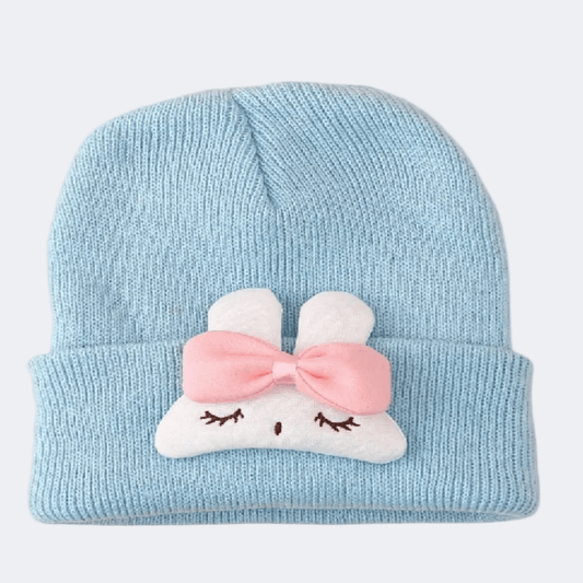 Light blue knit baby hat with a pink bow and white cloud design on a light gray background