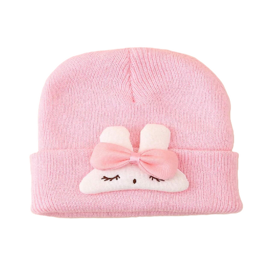 Pink knit baby hat with a cartoon face and bow on a white background