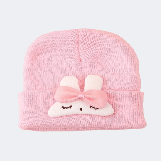 Pink knit hat with a cartoon cloud design and bow on a light gray background