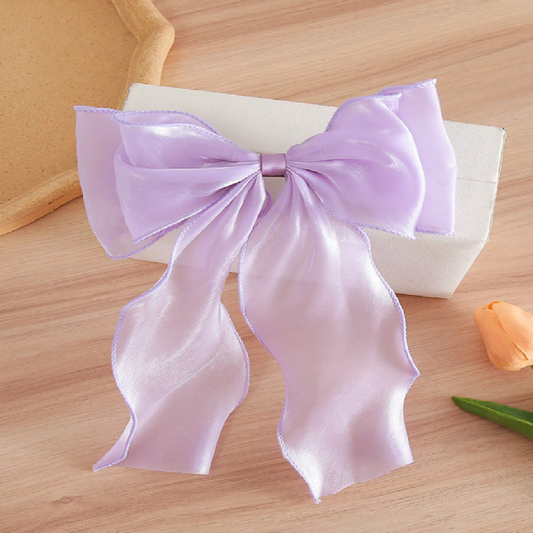 Large purple bow on a wooden surface with a white box and orange flower in the background