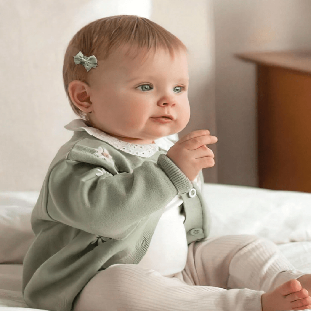 Baby in a light green jacket sitting on a bed