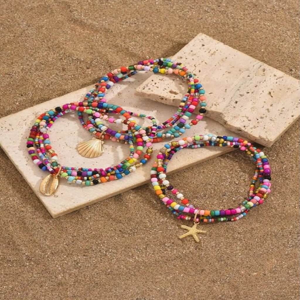 Colorful beaded bracelets with shell and starfish charms on a stone surface.