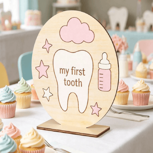 Decorative sign with 'my first tooth' text and baby bottle illustration on a stand, surrounded by cupcakes.